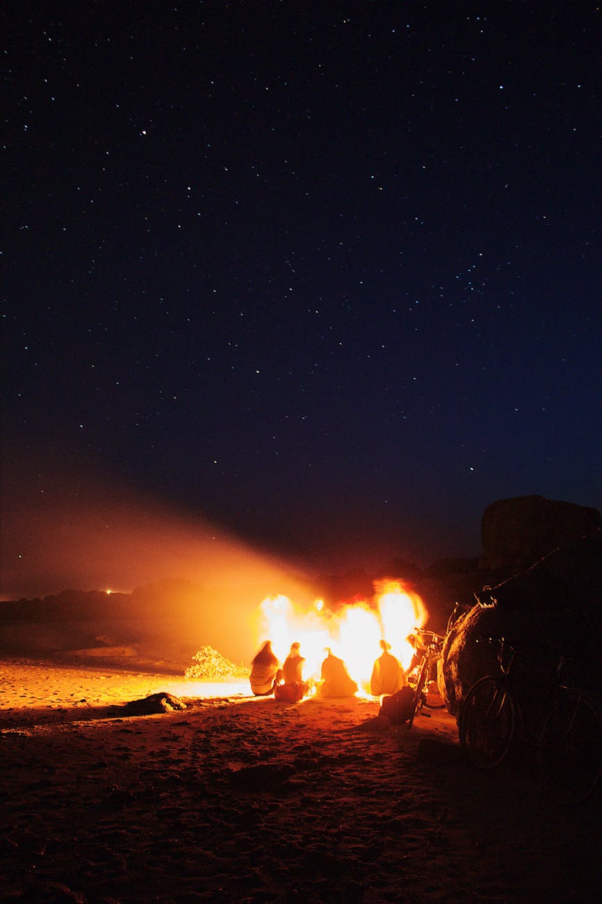 people gathered around a bonfire outdoors under starry night sky